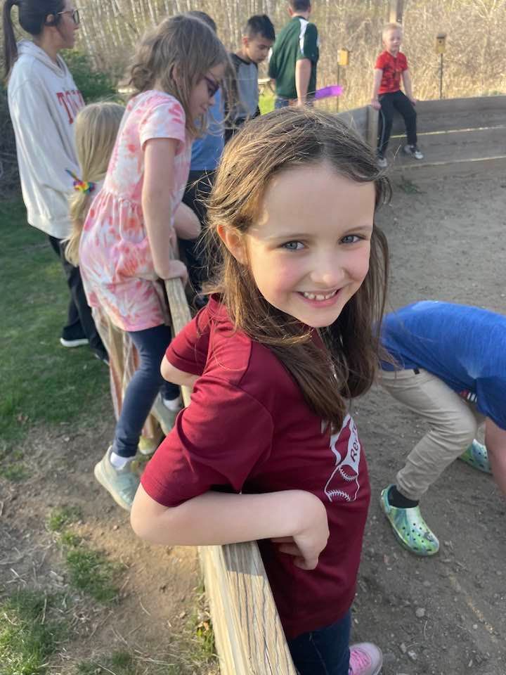 A little girl is leaning on a wooden fence and smiling.