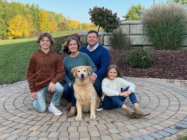 A family is posing for a picture with their dog on a brick patio.