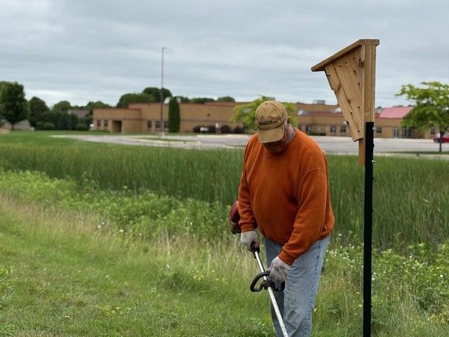 A man in an orange sweater is cutting grass with a lawn mower.