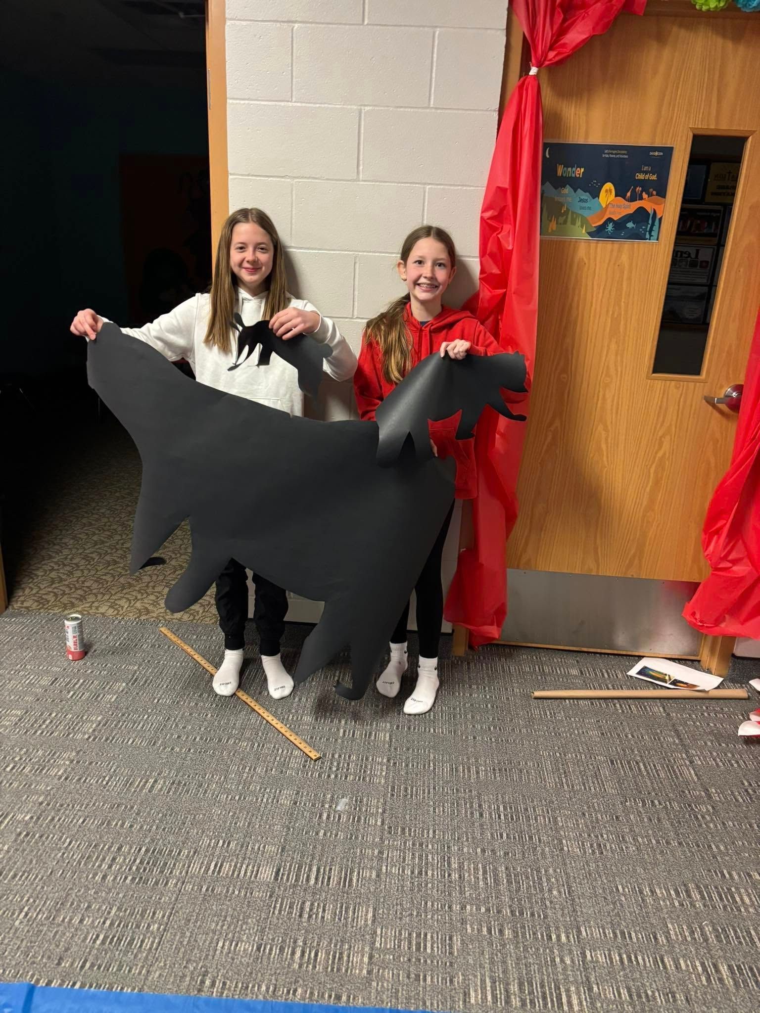 Two young girls are standing next to each other holding a large black animal.