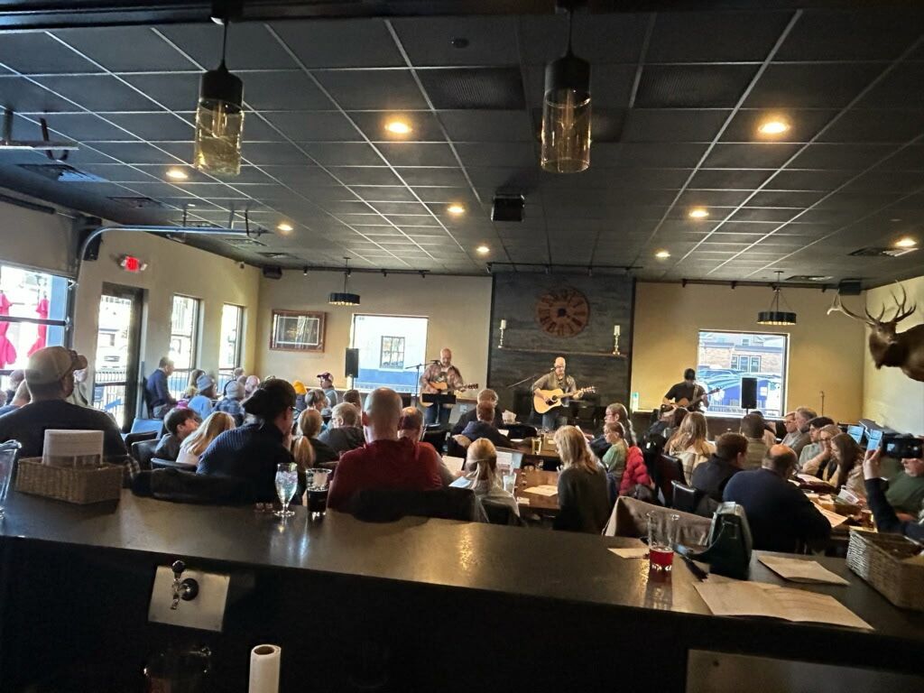 A group of people are sitting at tables in a restaurant watching a man play a guitar.