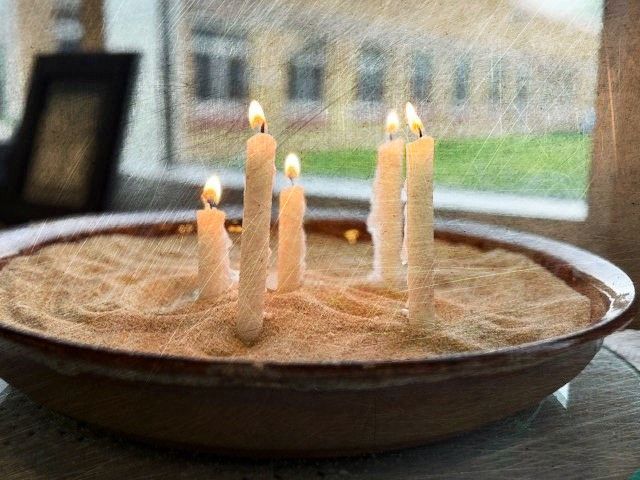 A bowl of sand with candles in it on a table.