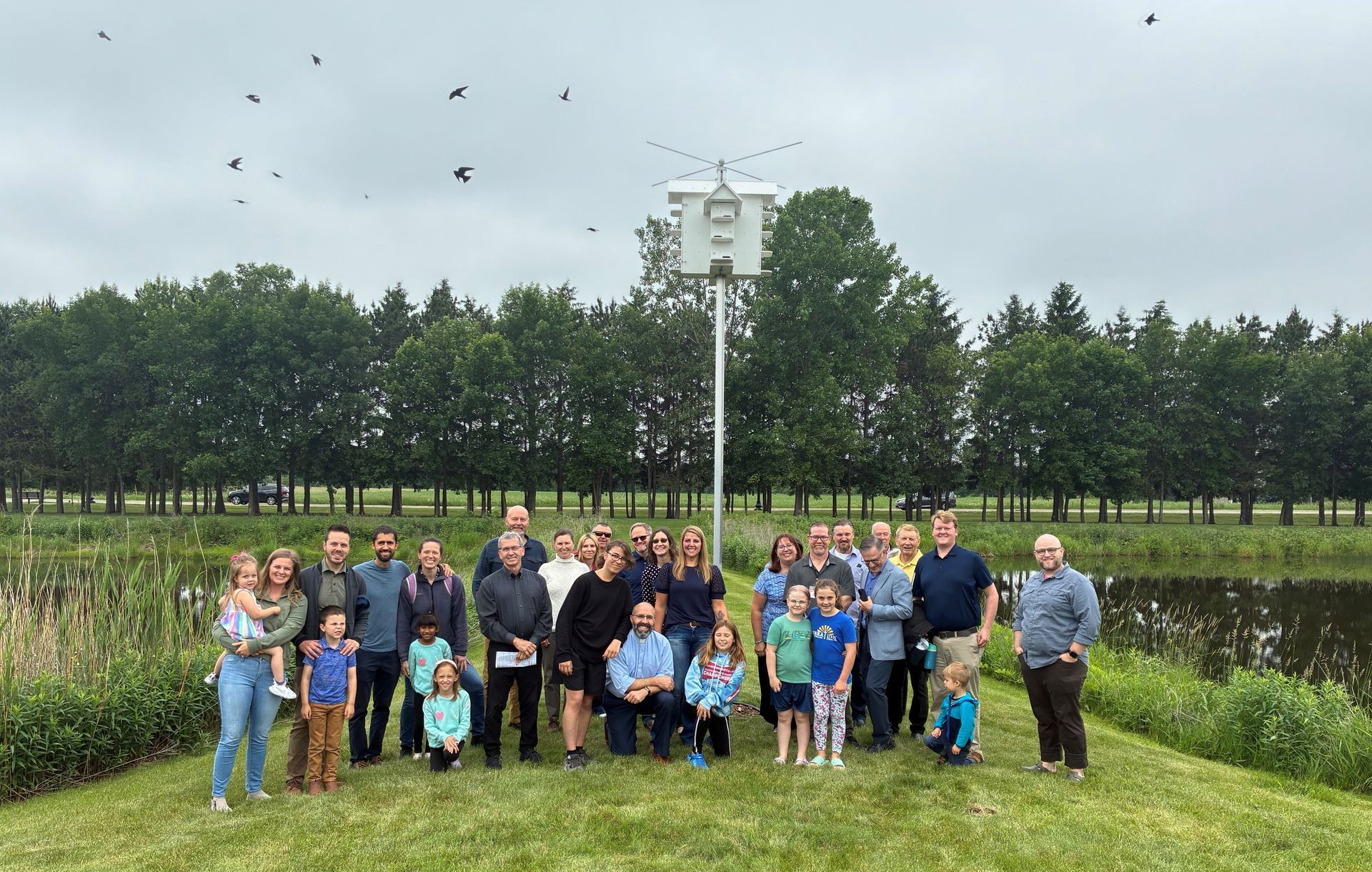 A large group of people are posing for a picture in front of a birdhouse.