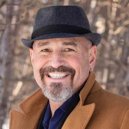 A man with a beard is wearing a hat and smiling.