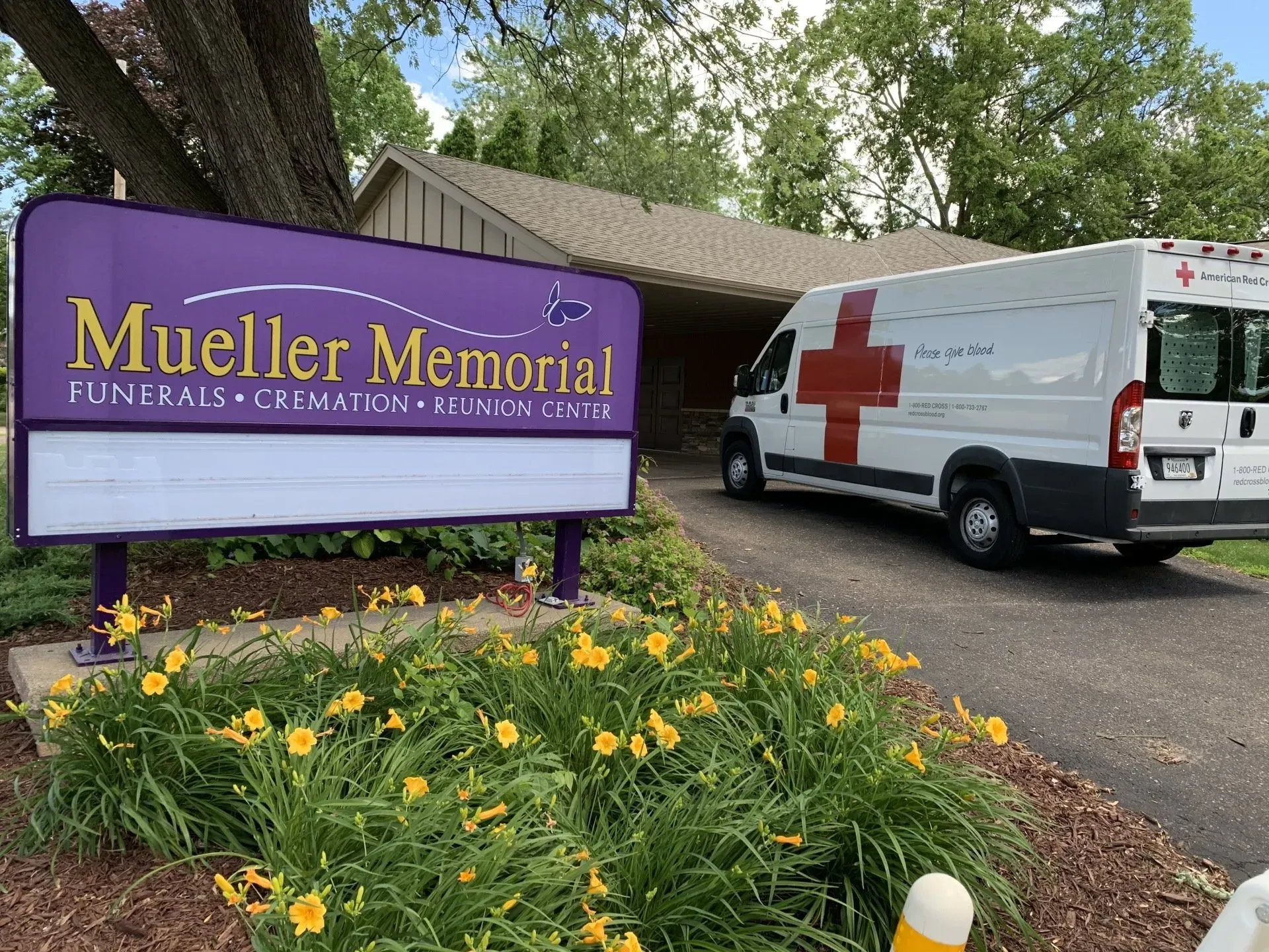 A white van with a red cross on it is parked in front of a funeral home.