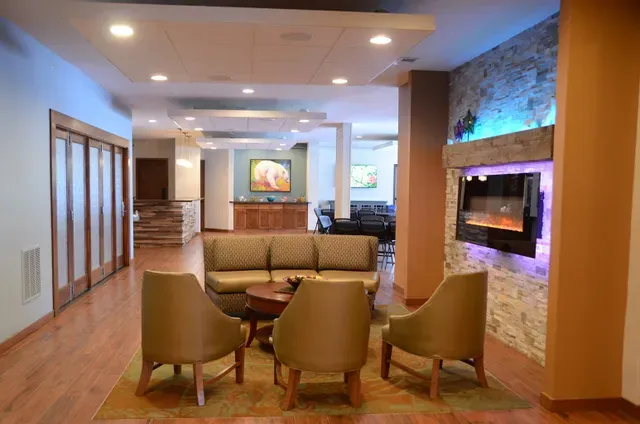 A hotel lobby with a couch , chairs , table and fireplace.