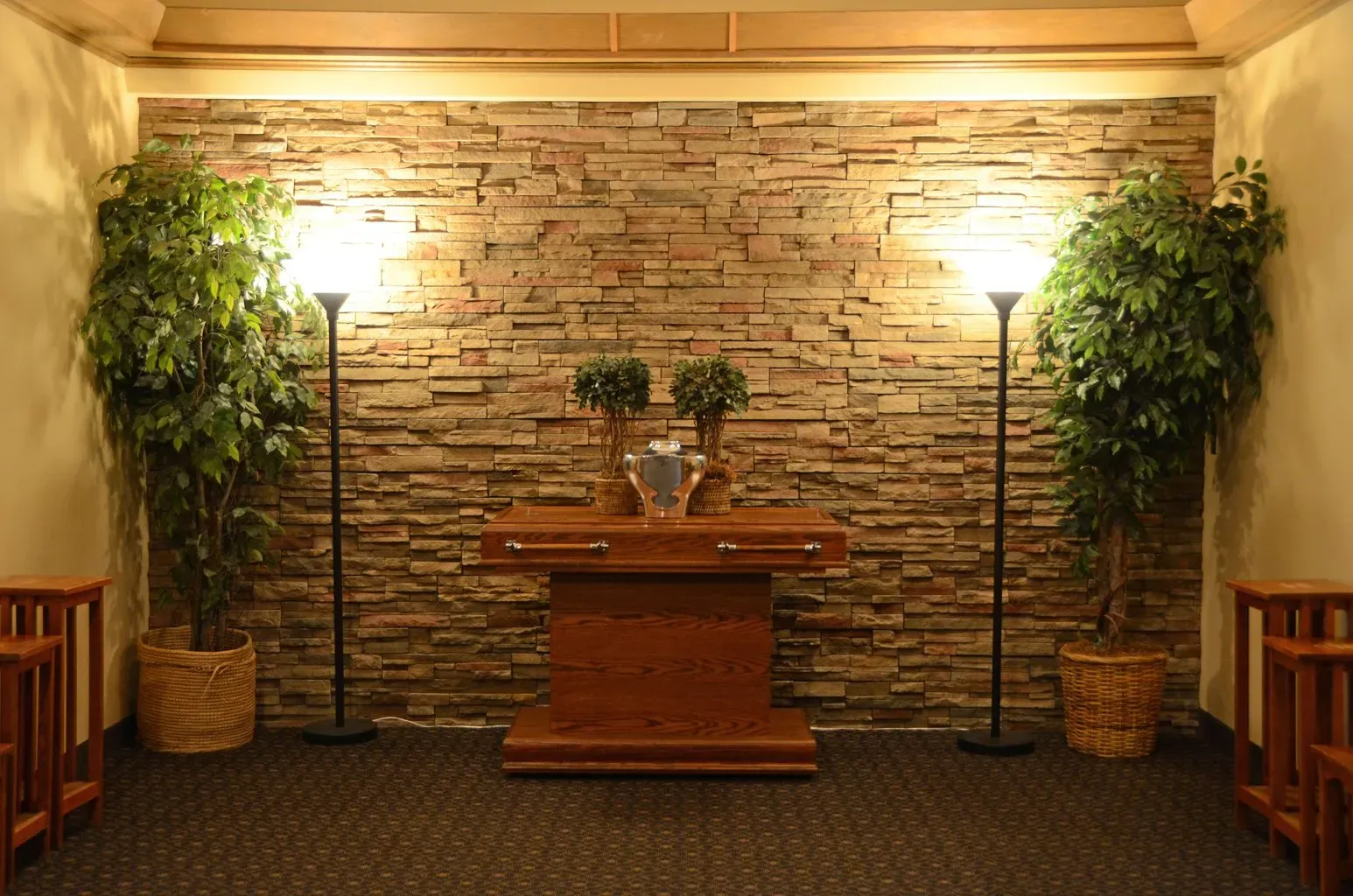 A room with a stone wall , a wooden table and two lamps.