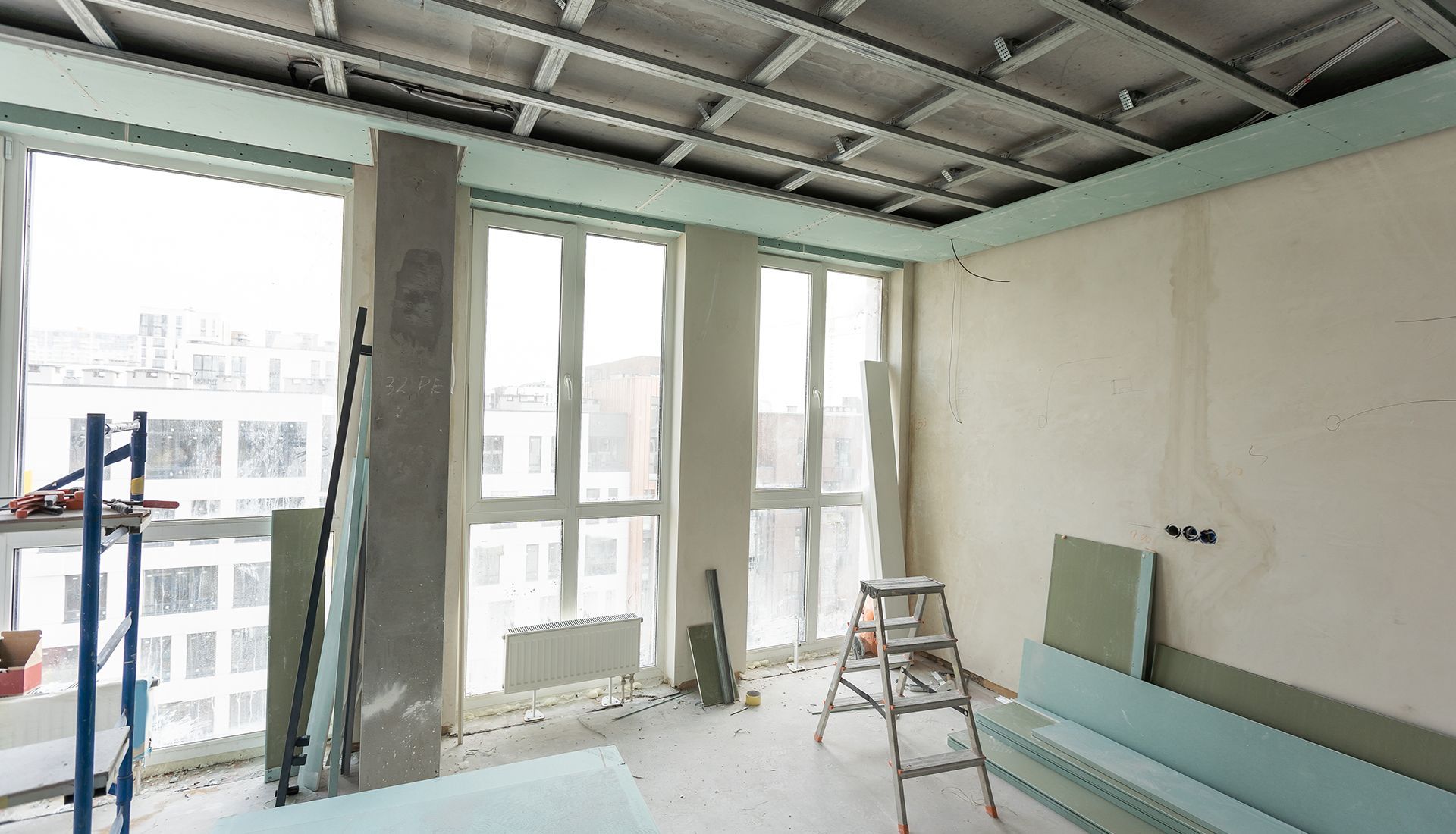 Interior of a room under construction with large windows, scaffolding, and building materials.