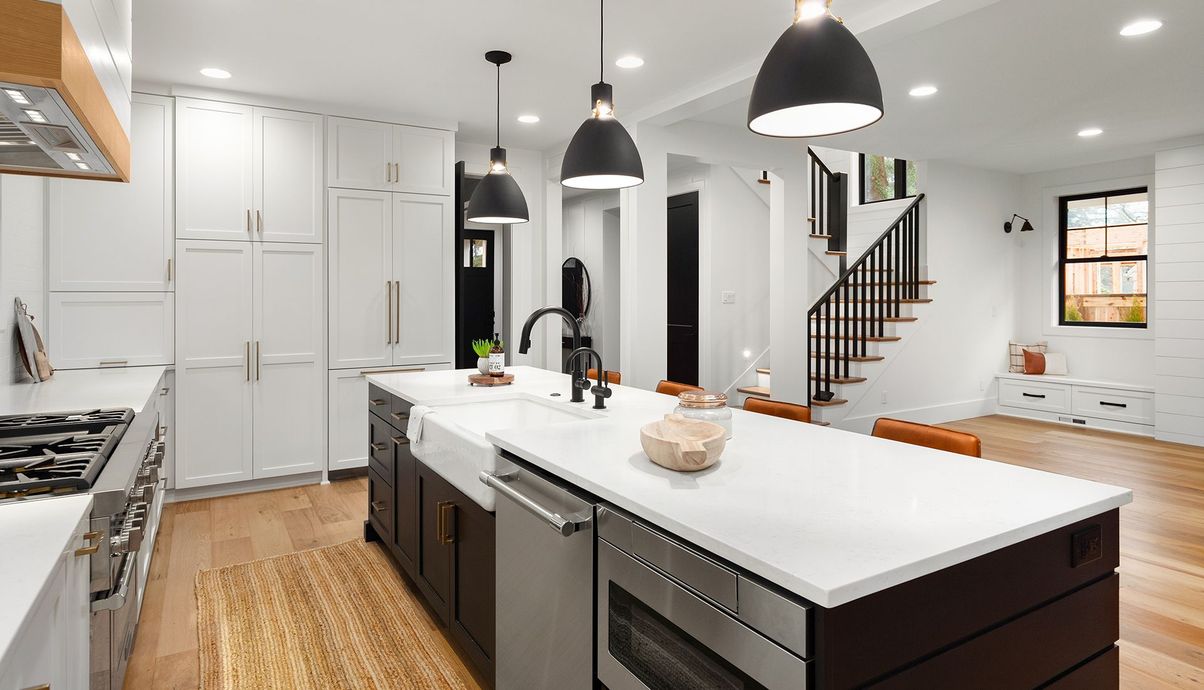Modern kitchen with white cabinets, island, dark pendants, and staircase.
