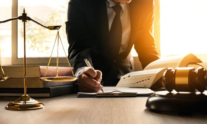 Lawyer writing, with scales of justice and gavel on a desk.