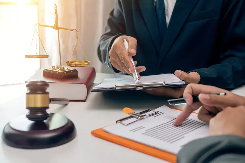 Two people in suits reviewing documents at a table. Gavel, scales, and law books present.