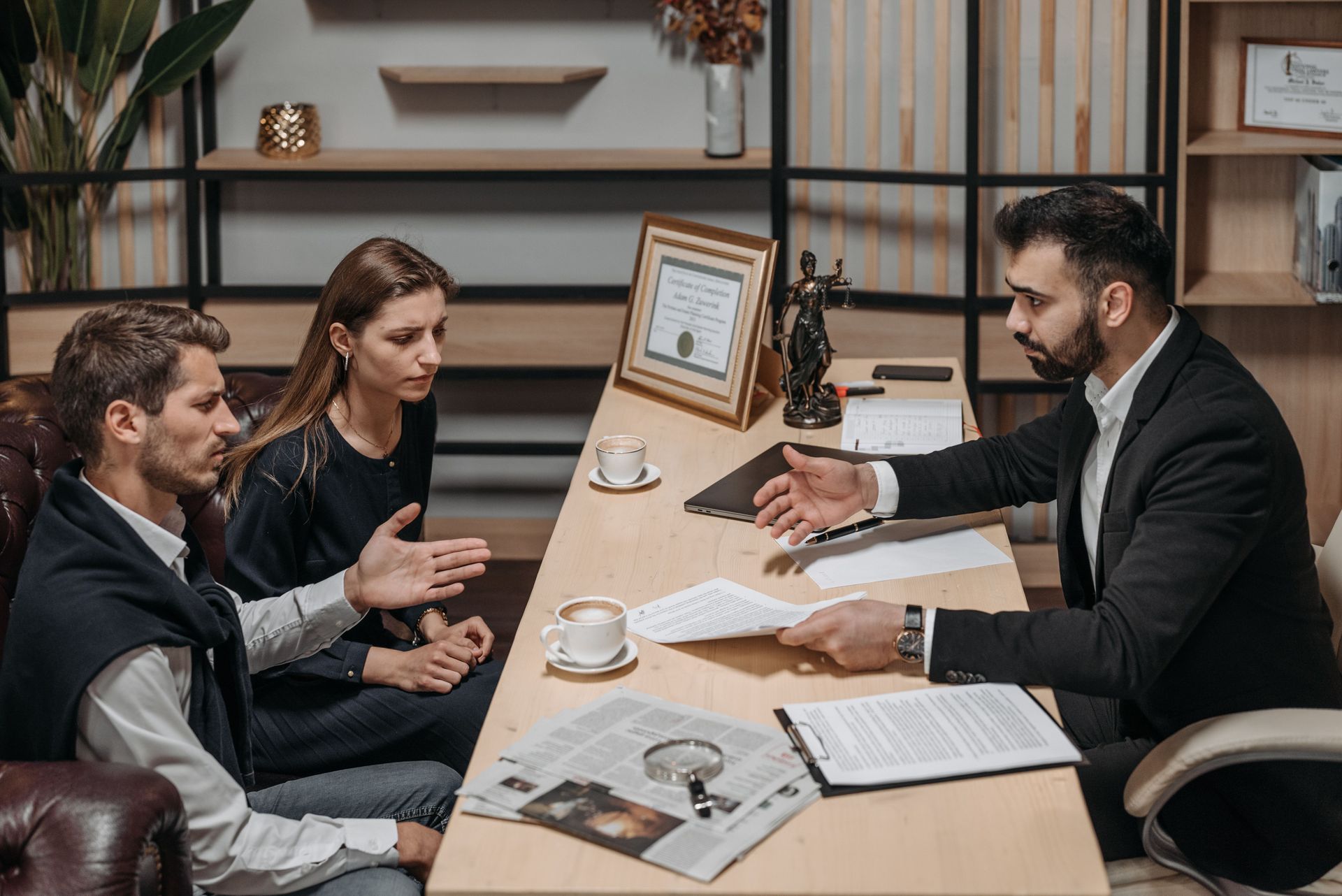 Three people in a meeting discussing documents across a wooden table in a modern office