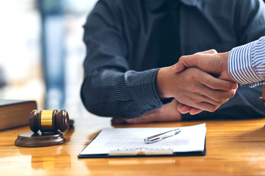 Two people shaking hands over a contract with a gavel on a wooden table.