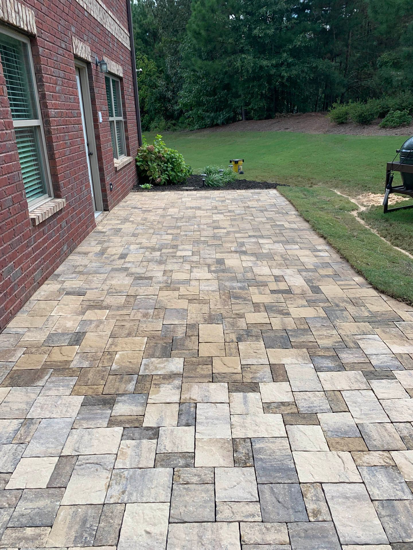 a brick walkway leading to a brick house with a grill in the backyard.
