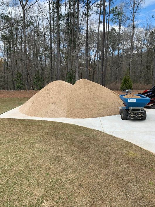 a pile of sand is sitting on the side of a driveway next to a dump truck.