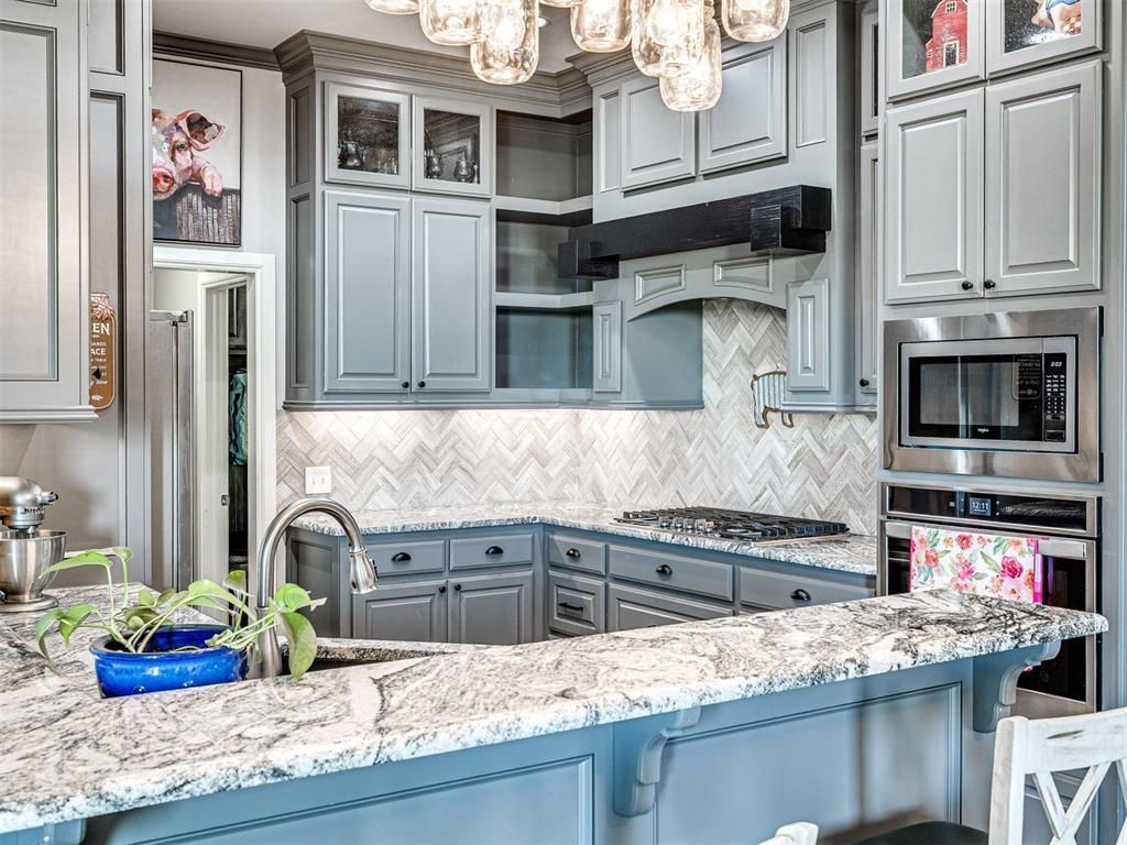 Modern kitchen with gray cabinets, granite island, chandelier, and stainless steel appliances
