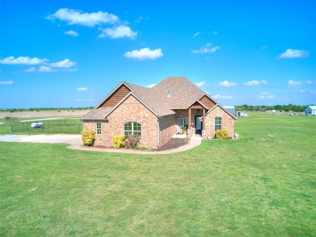 Brick house with a tan roof on a large green lawn under a bright blue sky