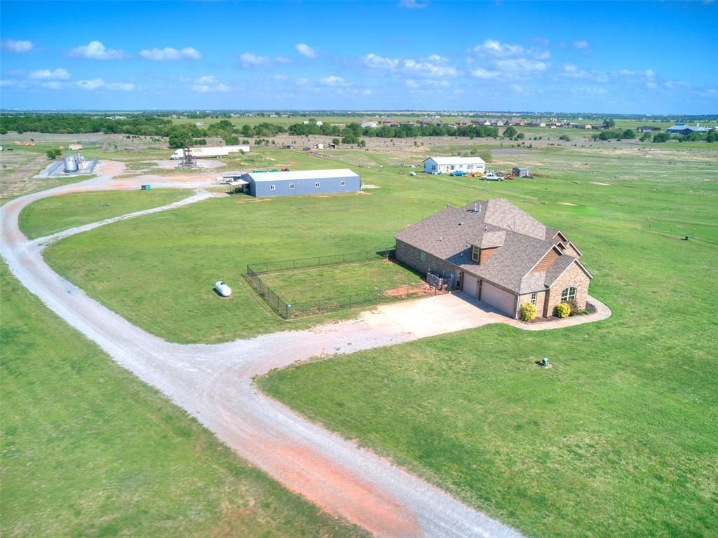 Aerial view of a rural farmstead with a barn, outbuildings, and green fields under a blue sky