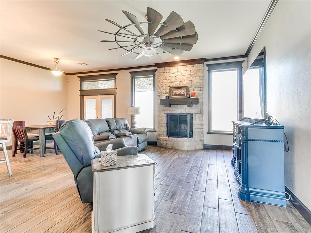 Bright living room with gray sofas, fireplace, large windows, and modern ceiling fan on wood floors.