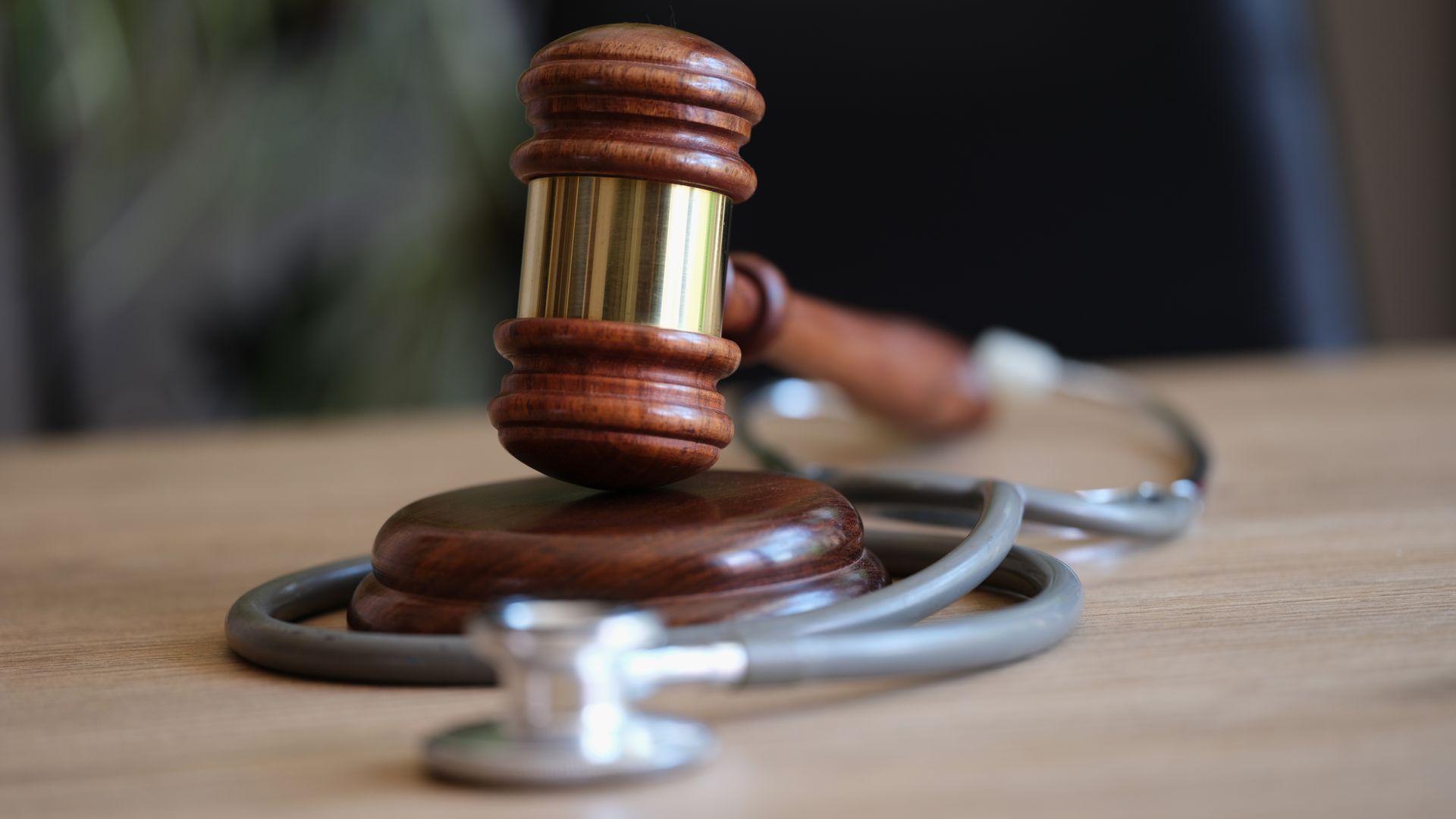 Wooden judge’s gavel resting on a stethoscope on a desk, symbolizing medical law and justice. Wooden judge’s gavel resting on a stethoscope on a desk, symbolizing medical law and justice.