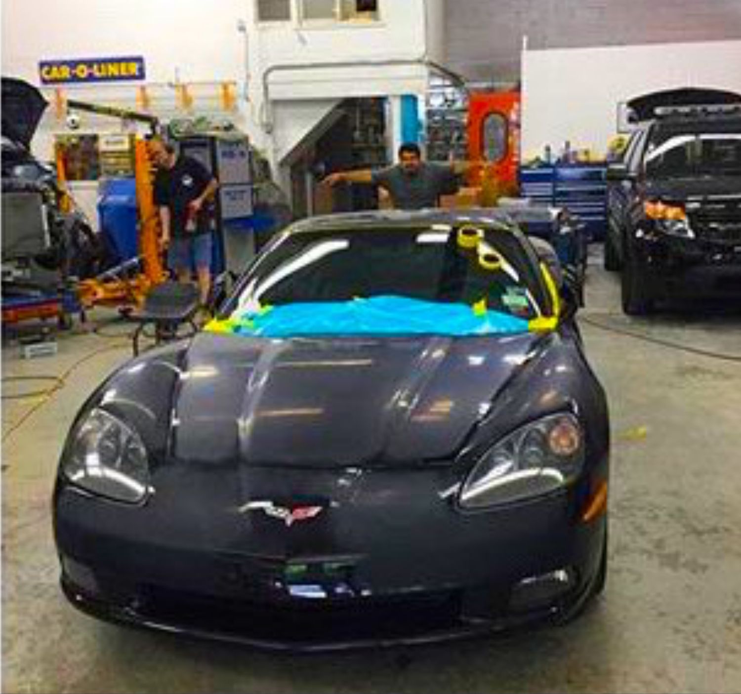 A black sports car is parked in a garage with a sign that says car-o-liner
