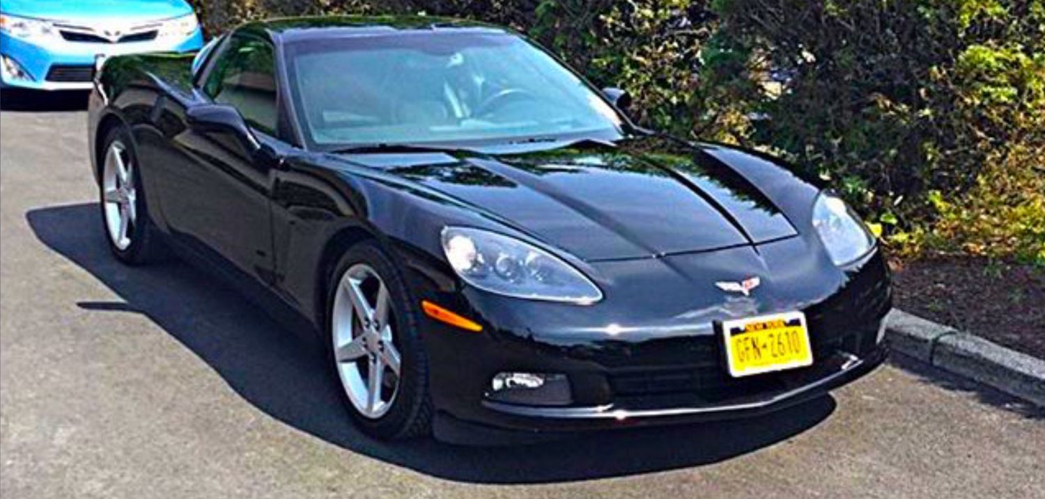 A black corvette is parked in a parking lot next to a blue car.