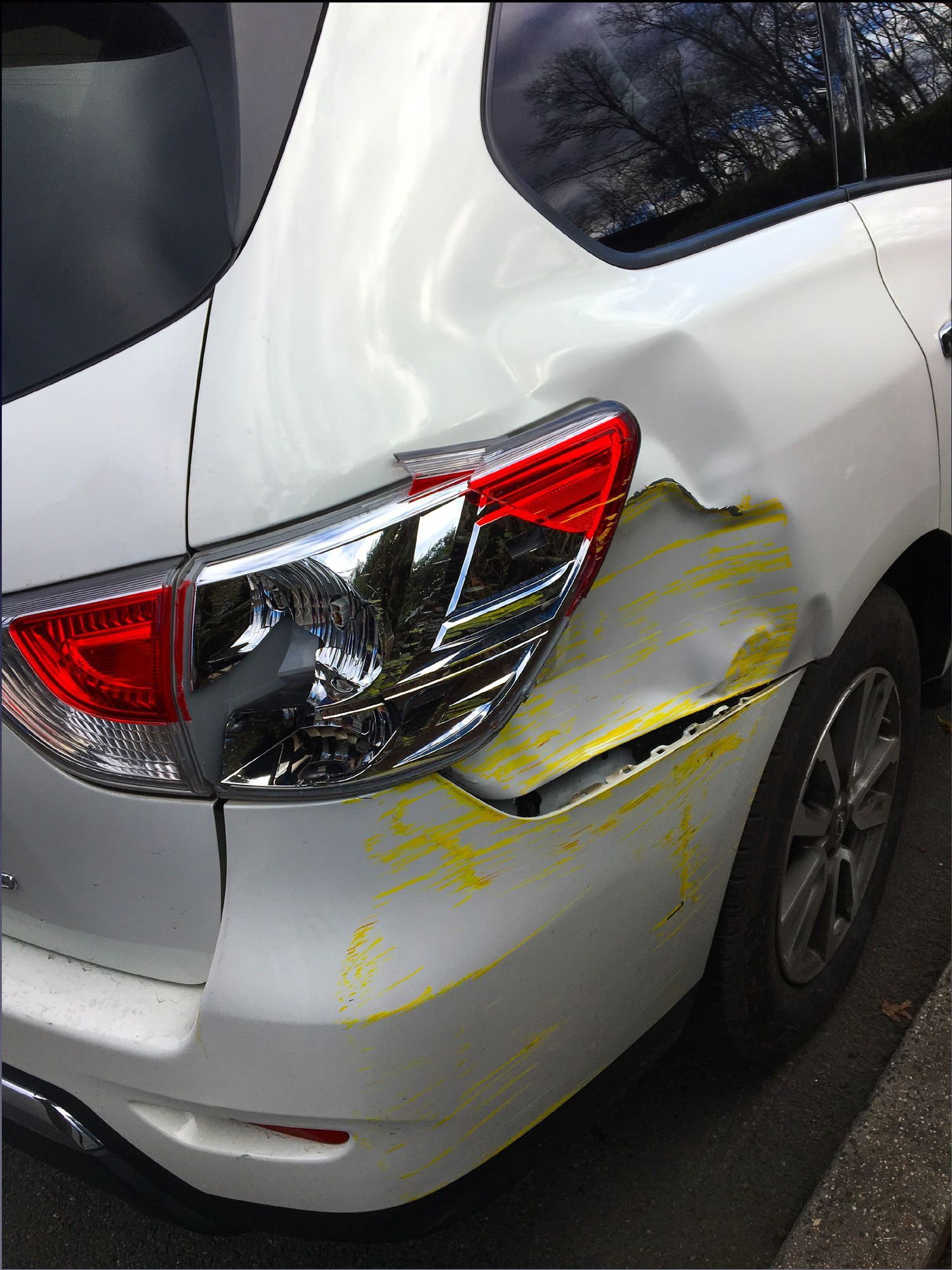 A white car with a damaged bumper is parked on the side of the road.