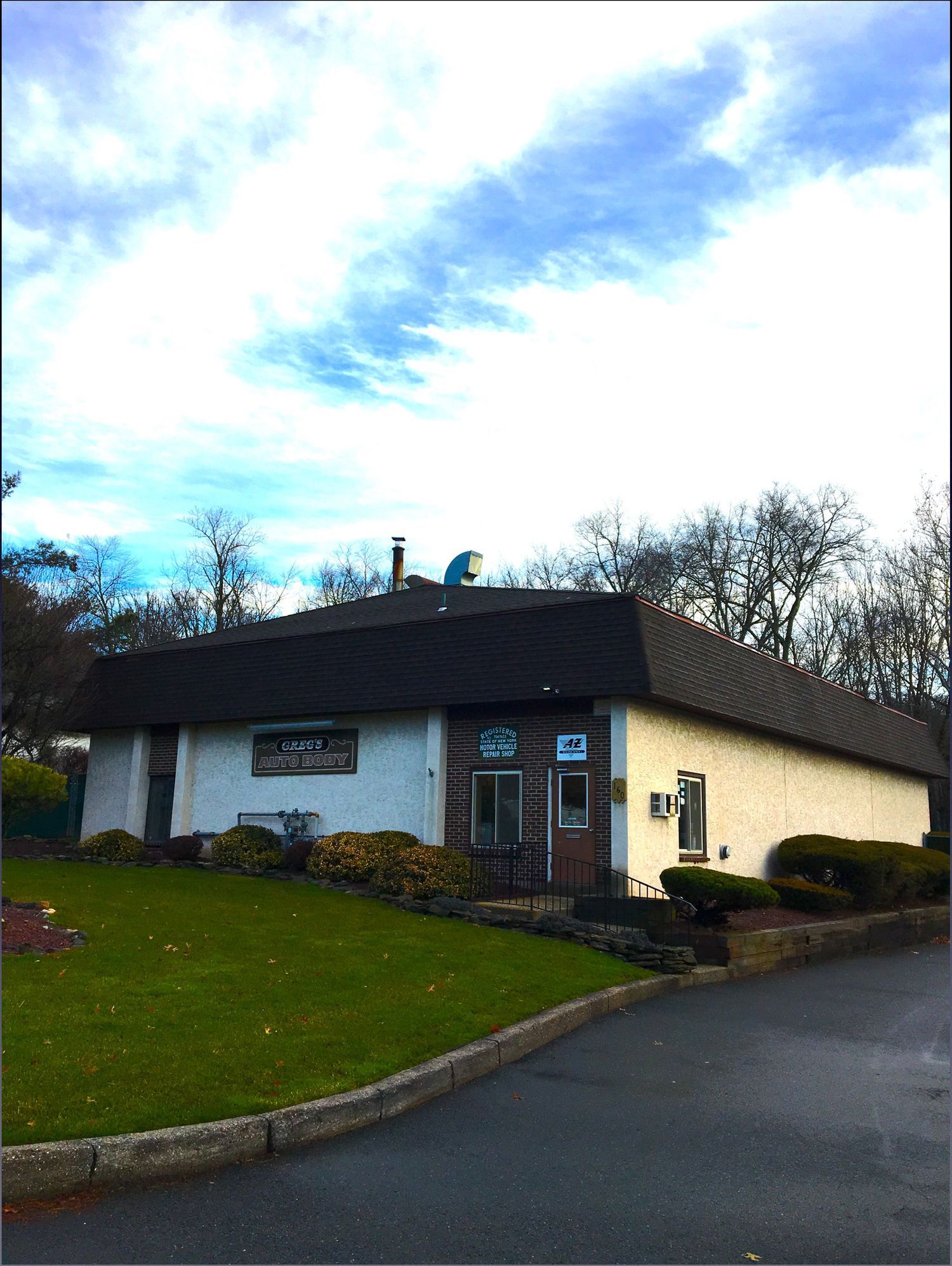 A white building with a black roof is surrounded by grass and trees