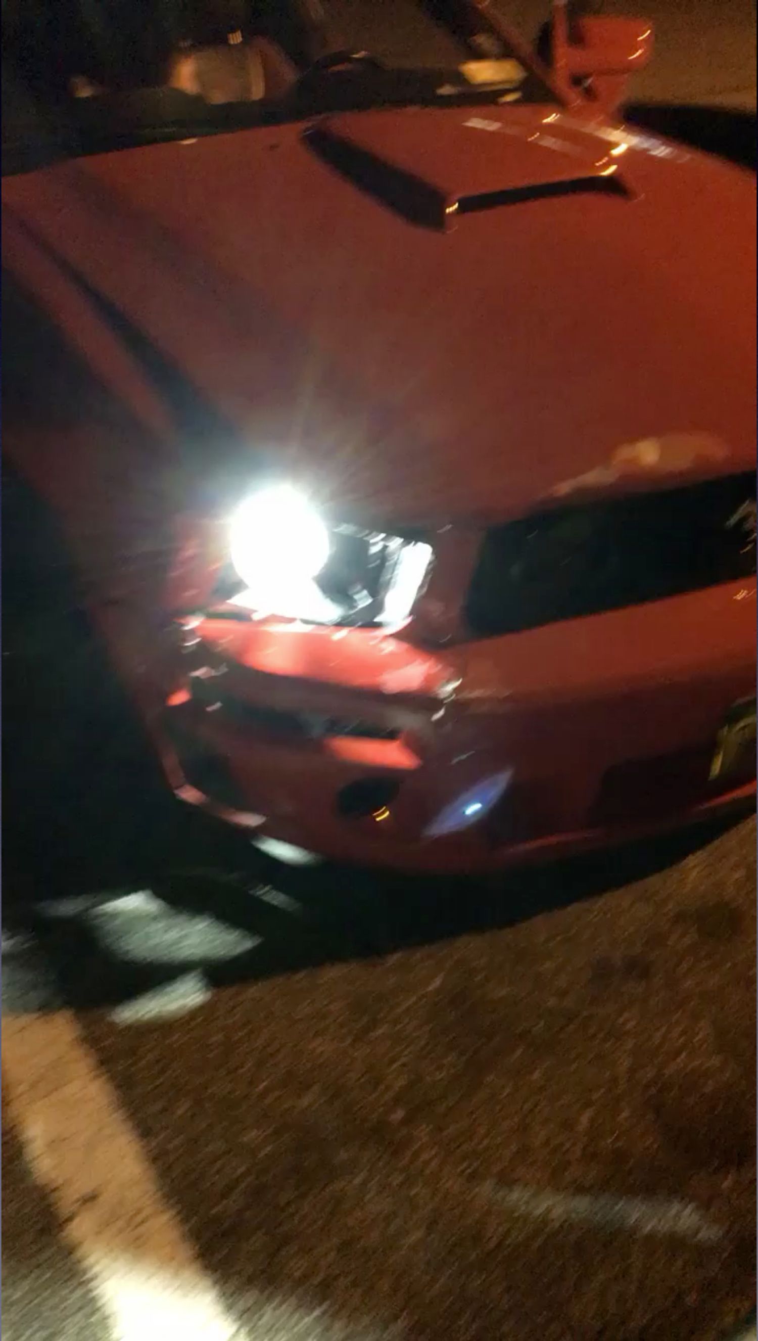 A red car is parked in a parking lot at night.