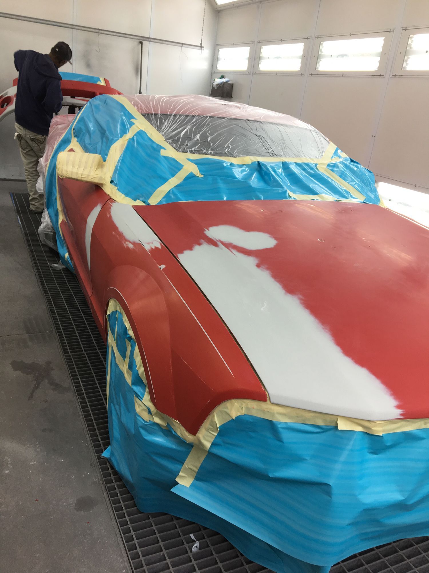 A red car is being painted in a paint booth.