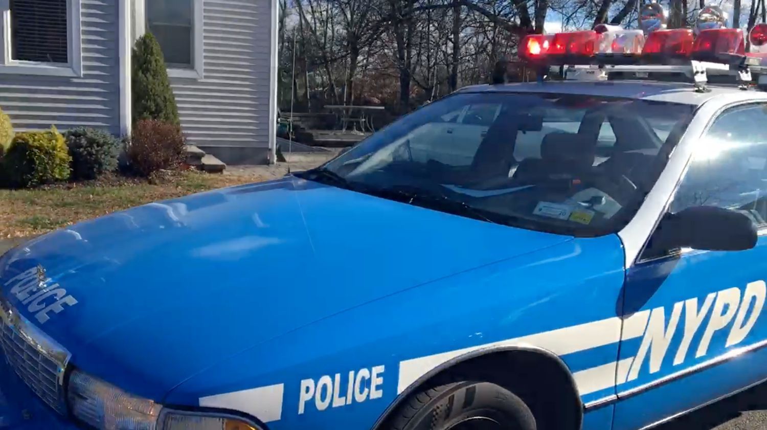 A blue and white police car is parked in front of a house.