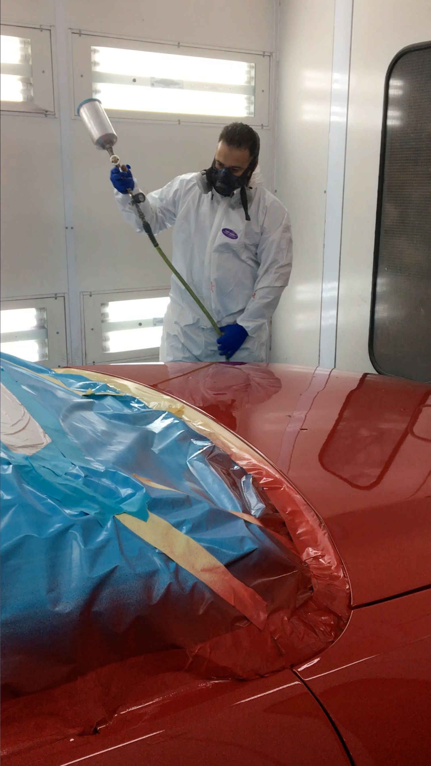 A man is spray painting a red car in a paint booth.