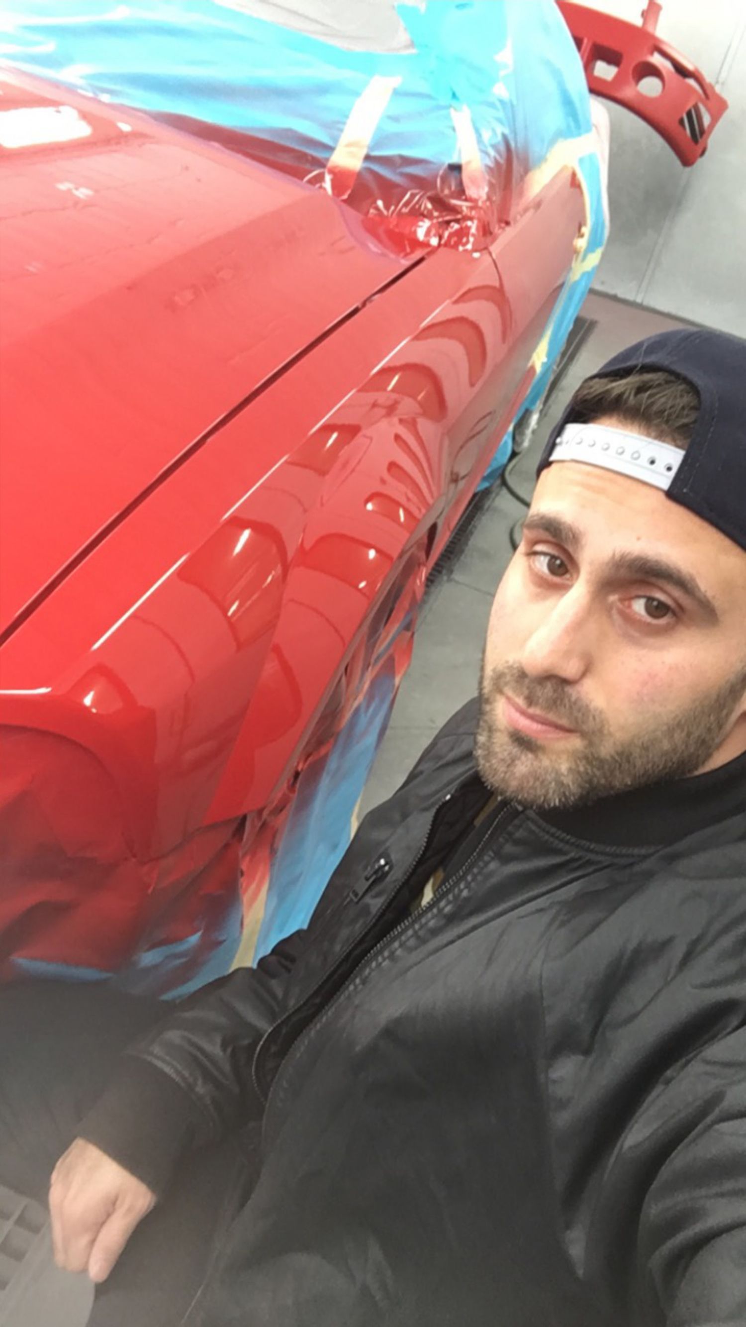 A man is taking a selfie in front of a red car.