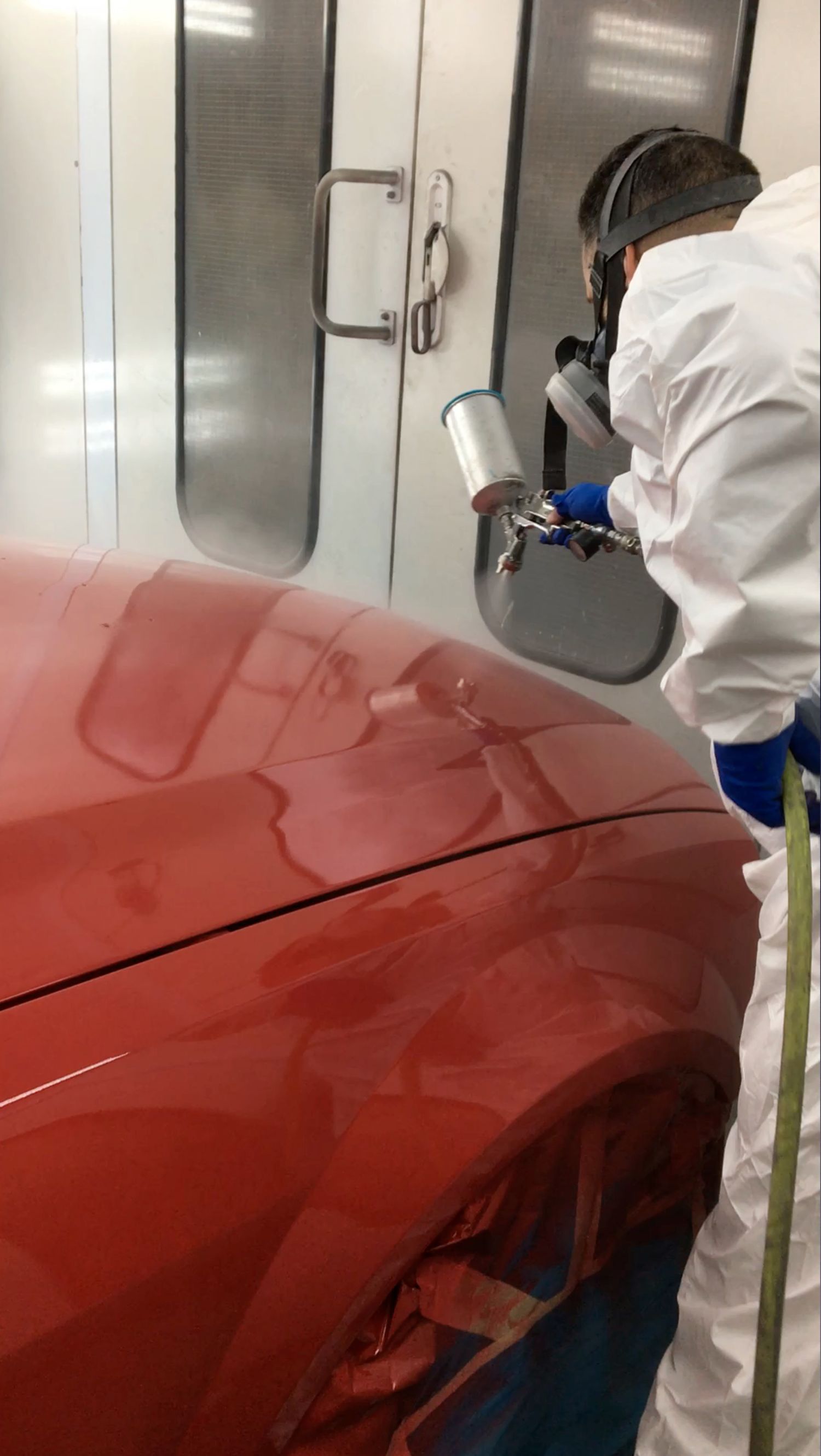 A man is spray painting a red car in a paint booth.