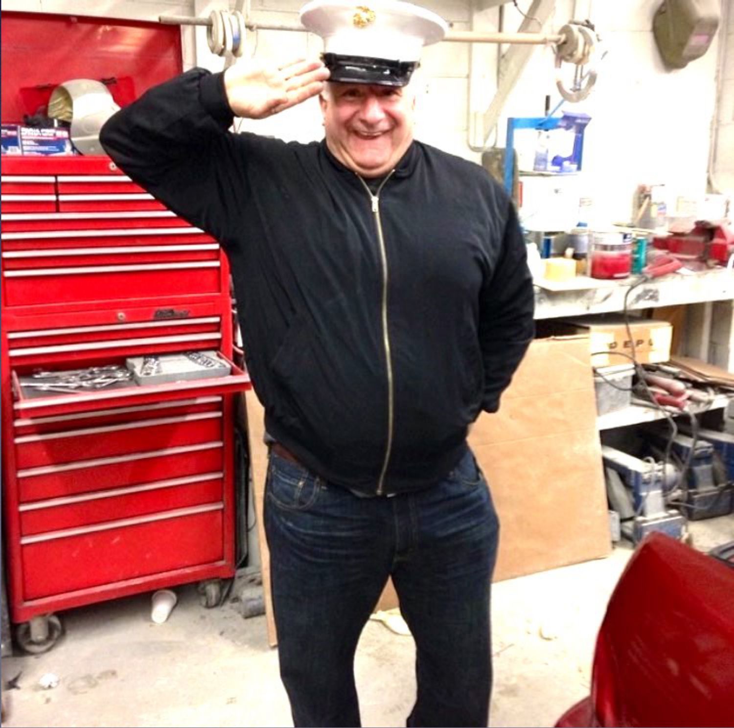 A man wearing a military hat salutes in front of a red toolbox