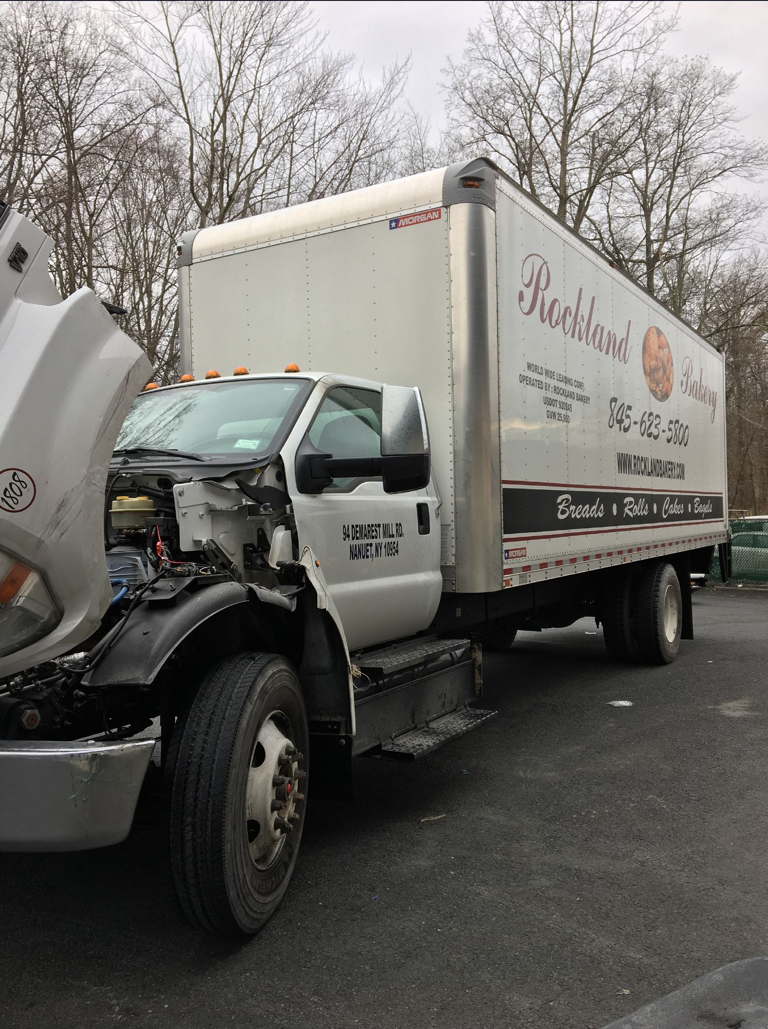 A white truck with the hood open is parked in a parking lot
