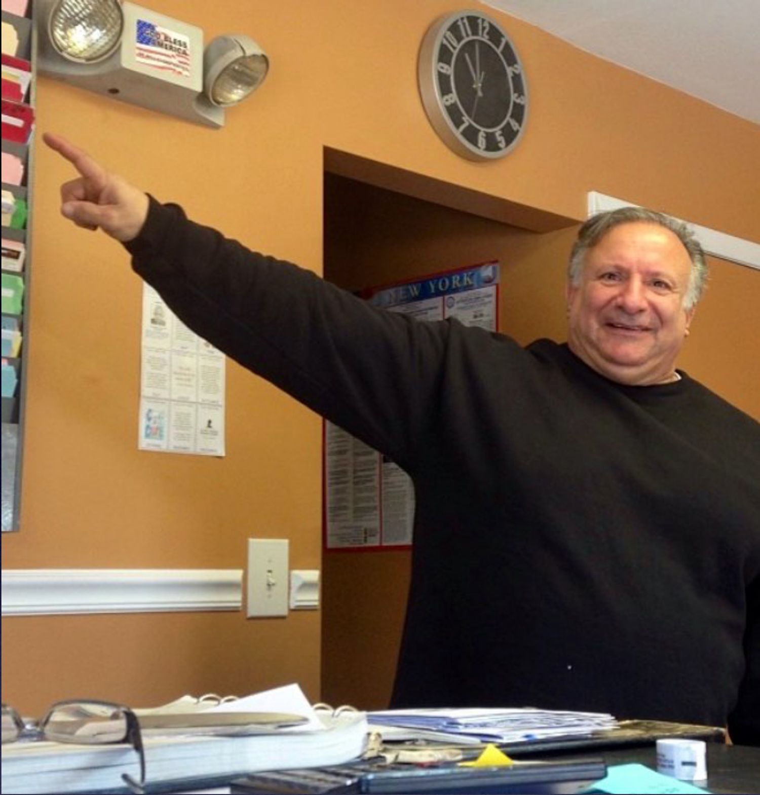 A man in a black shirt points to a clock on the wall