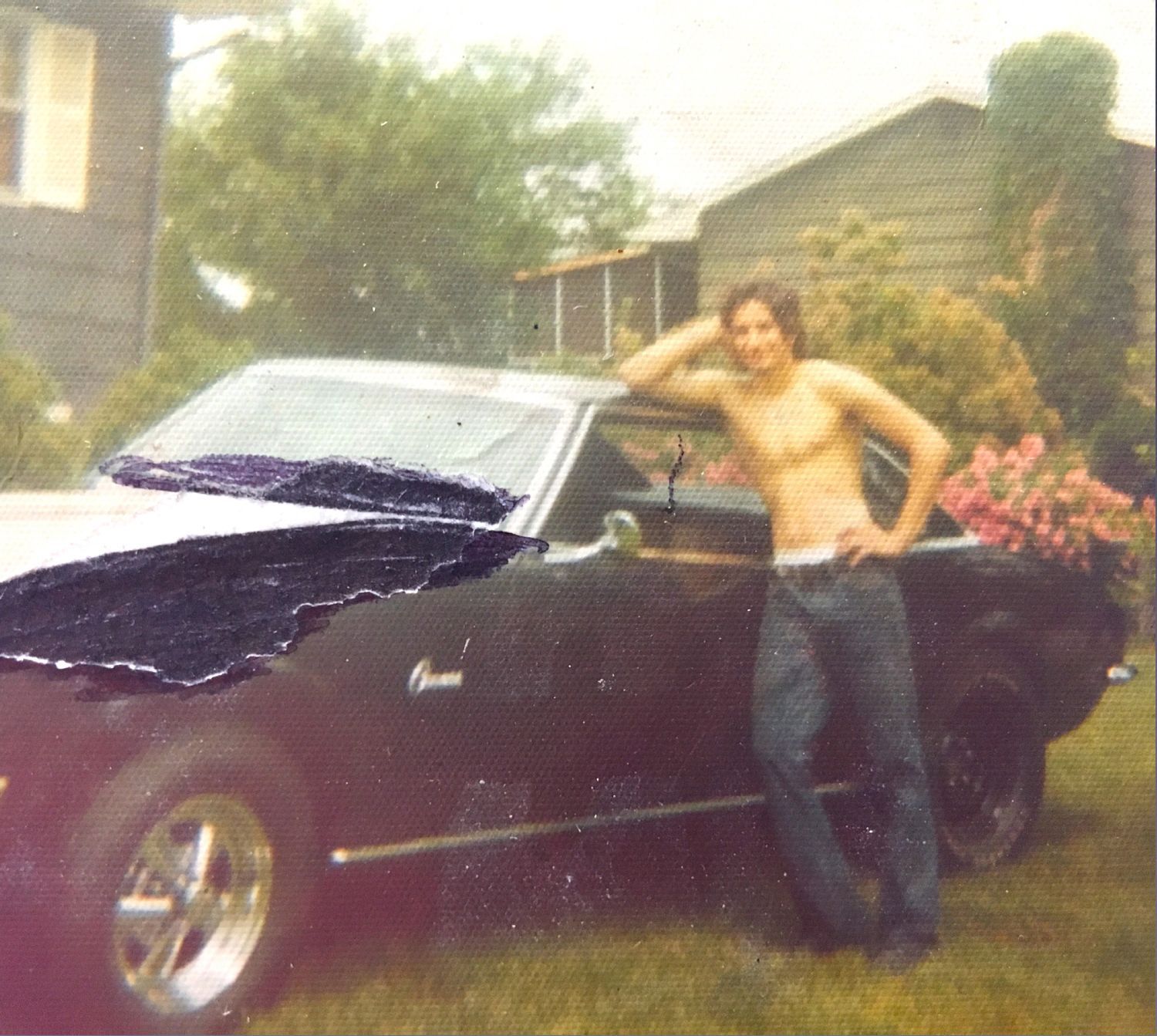 A shirtless man stands in front of a black car