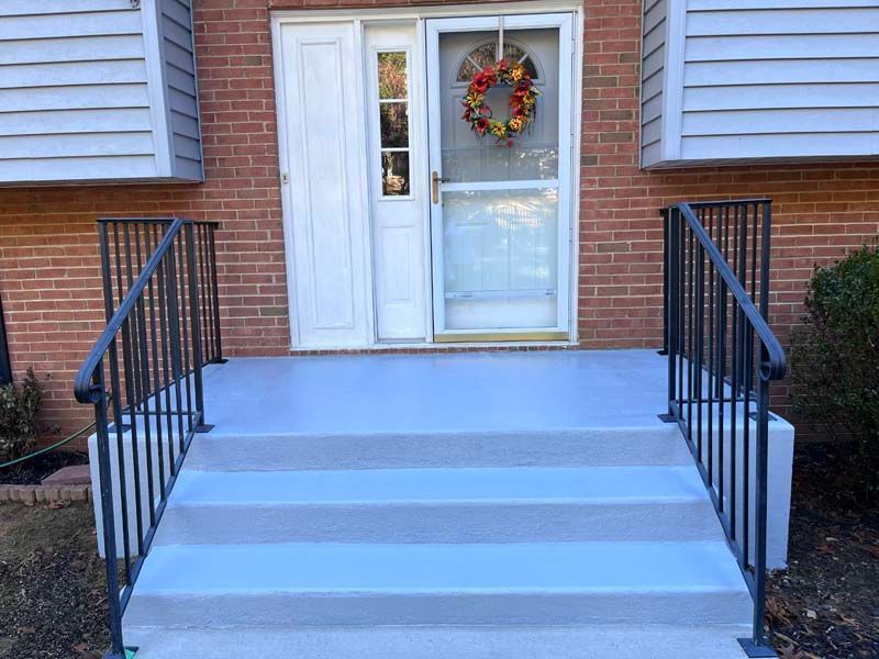 Gray painted porch with three steps leading to a white door with a screen and wreath; black railings