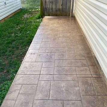 Concrete walkway with a stone pattern next to a grassy area and a house with white siding