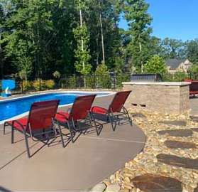 Poolside scene with red lounge chairs, outdoor kitchen, and swimming pool