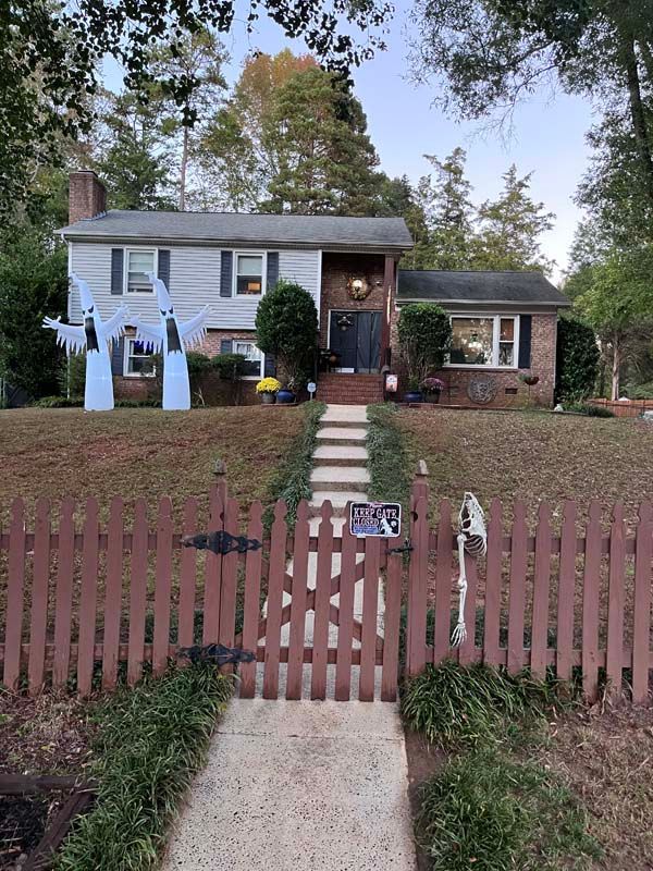 A two-story house decorated for Halloween with ghosts, a fence, and a walkway
