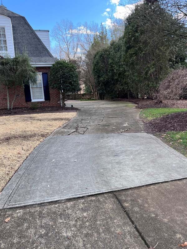 Driveway leading to a brick house with trees on either side under a blue sky