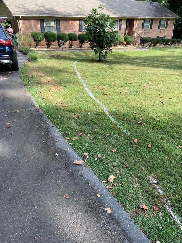 White painted line on green lawn next to asphalt driveway, leading to a brick house