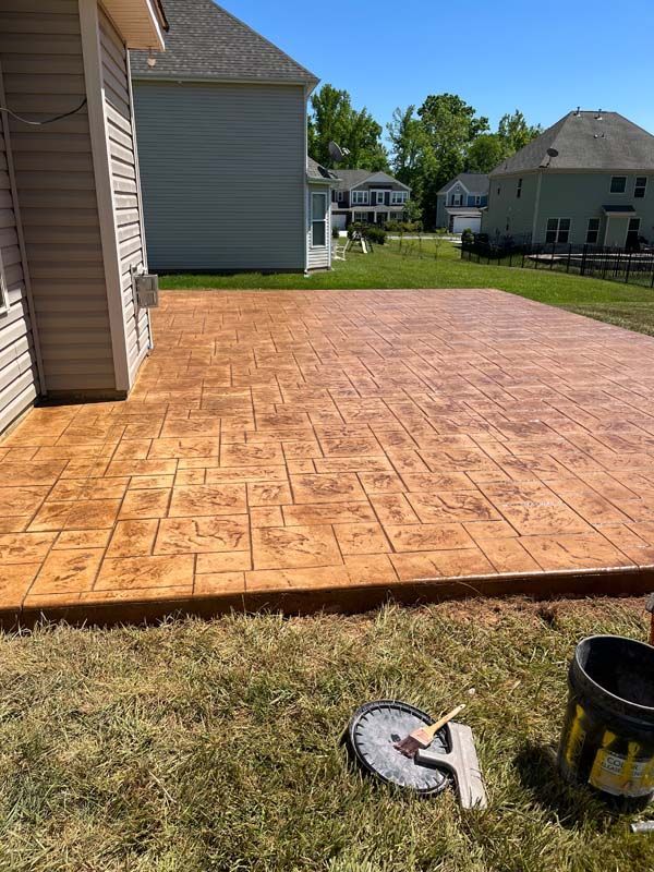 Stamped concrete patio in brown hues with tools on grass next to a house
