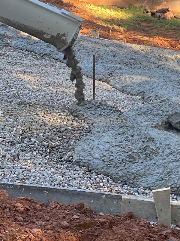 Concrete being poured onto gravel, forming a pathway with wooden borders in an outdoor setting