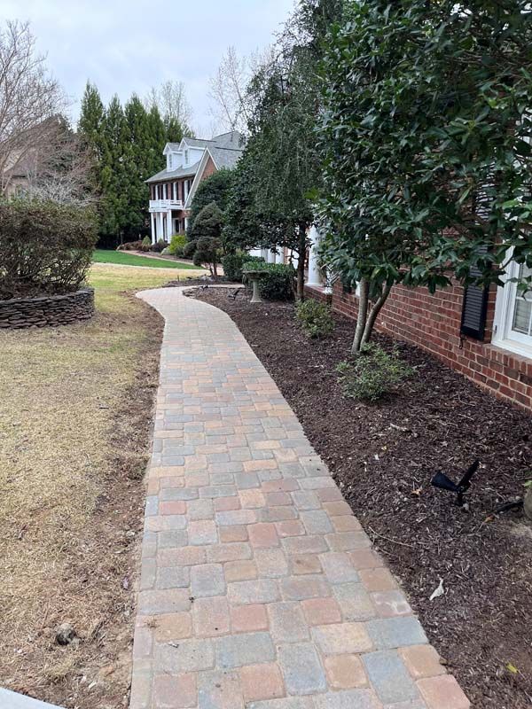 Brick path leading to a house with a grassy lawn and trees