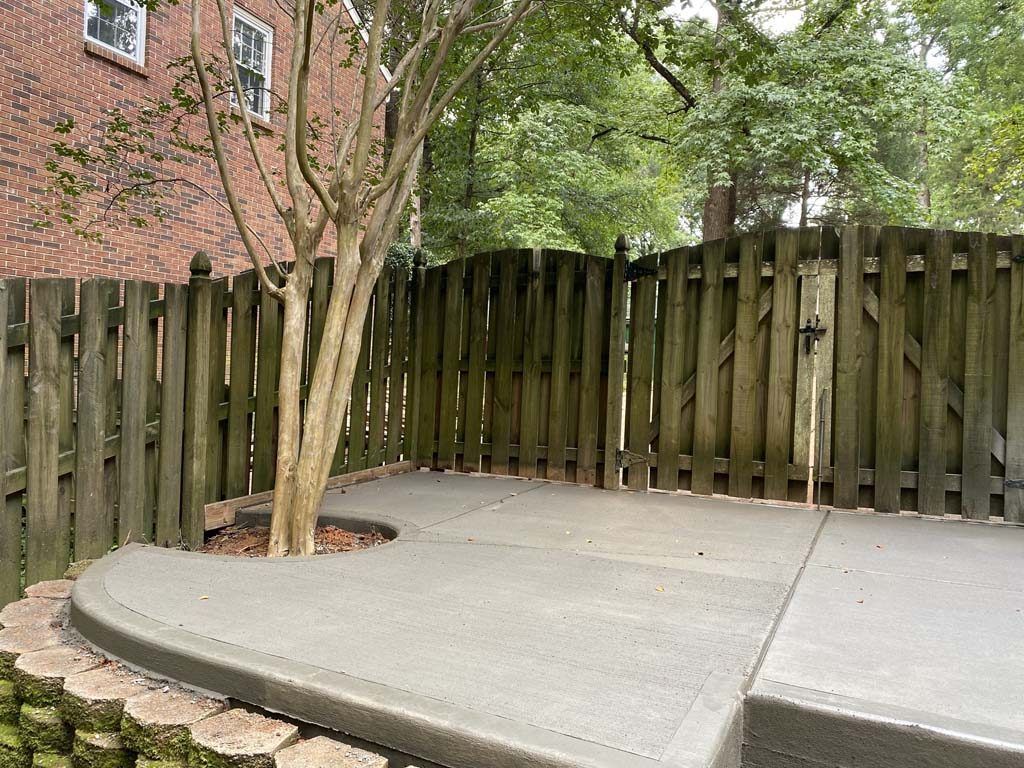 Concrete patio next to a tree, bordered by a wooden fence and brick wall