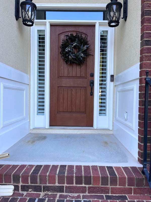 Brown front door with wreath, sidelights, and brick steps