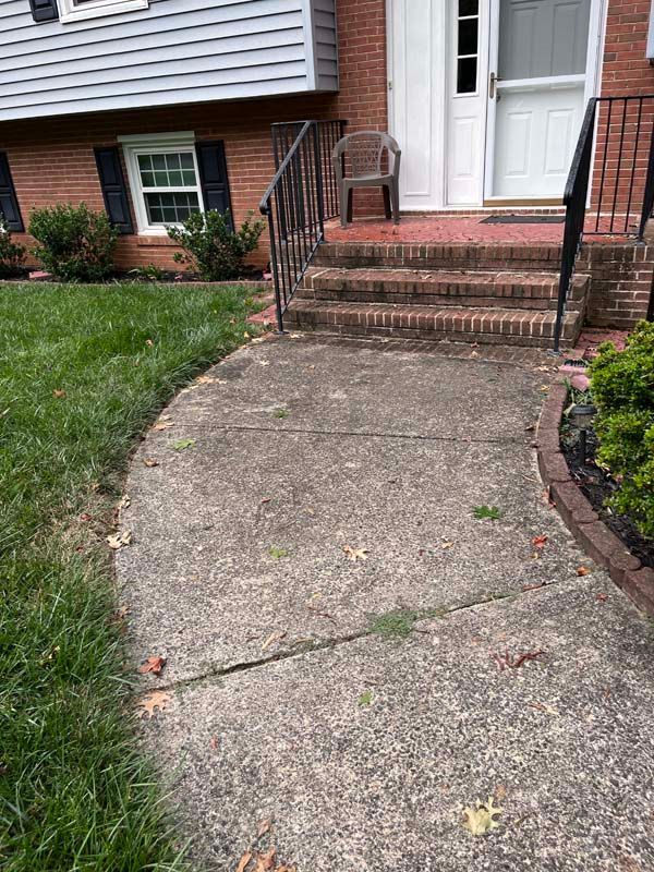 Concrete walkway leading to a brick-stair entrance of a brick house with a front lawn